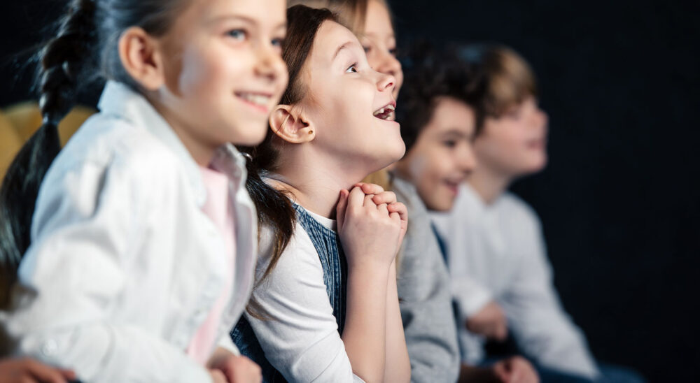 Niños mirando con asombro y alegría hacia un escenario de teatro