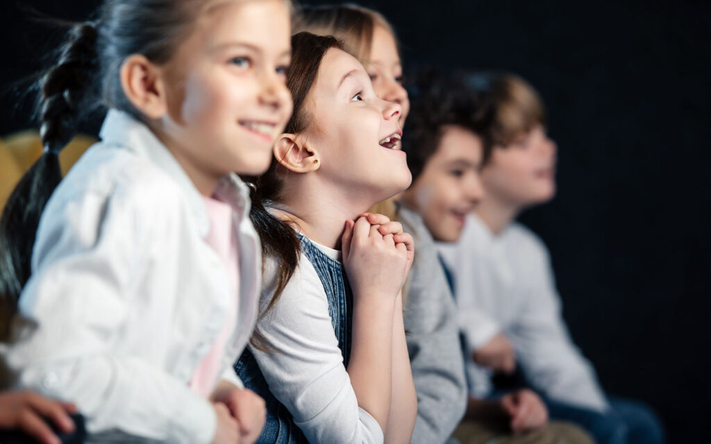 Niños mirando con asombro y alegría hacia un escenario de teatro