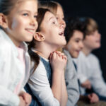 Niños mirando con asombro y alegría hacia un escenario de teatro
