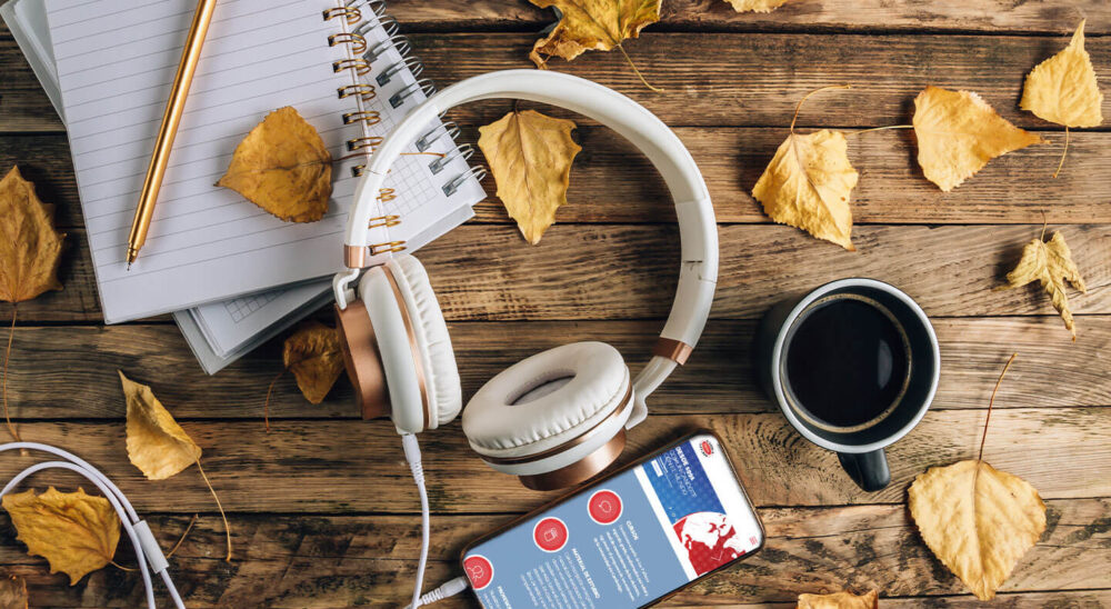 Auriculares, cuaderno, café y un móvil con una web de cursos sobre una mesa de madera con hojas secas de otoño