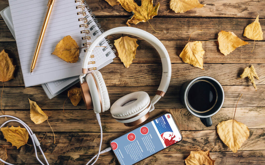 Auriculares, cuaderno, café y un móvil con una web de cursos sobre una mesa de madera con hojas secas de otoño