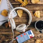 Auriculares, cuaderno, café y un móvil con una web de cursos sobre una mesa de madera con hojas secas de otoño